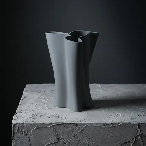 Labyrinth in Slate: a vase of folded tubes on a rough plaster block against a dark wall