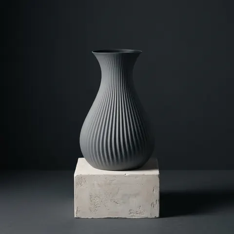 Otto in Slate: a ribbed bottle vase on a plinth in a dark studio